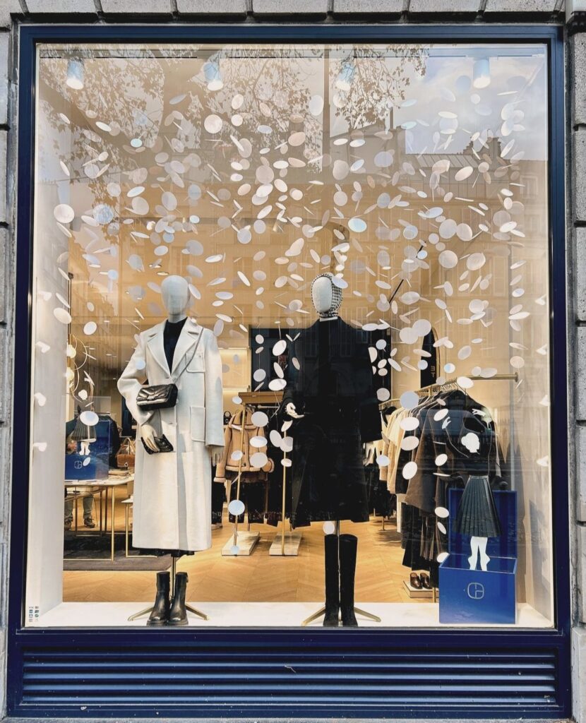 Vitrine de Noël du flagship Claudie Pierlot à Paris, décorée de guirlandes de cercles blancs et d’une danseuse au jupon noir en papier plissé.