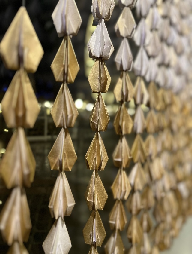 Détail de nombreux modules en papier doré composant une installation linéaire.